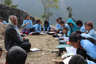 Students studying outdoors on a hillside with their teacher.